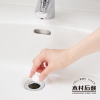 一只手正在將一顆白色、圓形的排水管清潔錠放入白色陶瓷水槽的排水孔。