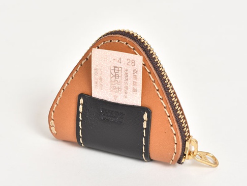 棕色皮革製成的職人手作零錢包，造型為三角飯糰。正面有一個黑色皮革小口袋，露出部分粉紅色日文票券。零錢包配有黃銅色拉鍊，縫線為米白色。