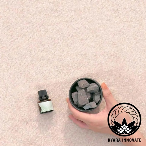 KYARA INNOVATE 品牌下，一個小瓶裝精油旁，手持一個裝有灰色擴香石的黑色小碗。