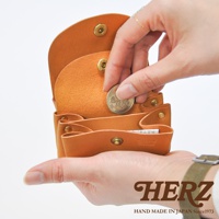 一只手正在將一枚硬幣放入一個棕褐色皮革製成的三層收納零錢包。零錢包上有金屬按扣。