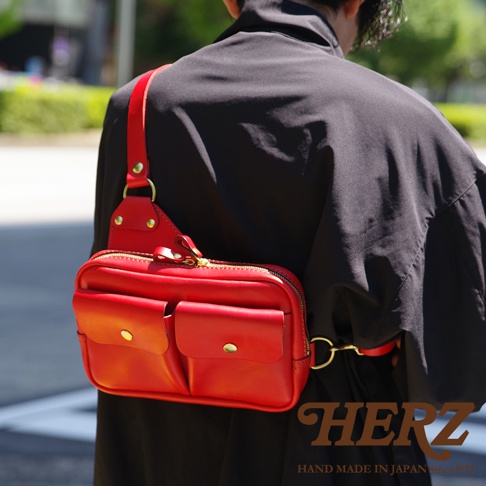 鮮紅色皮革雙口袋斜背包，附有拉鍊主袋，正面兩個翻蓋口袋，金屬扣環，肩帶可調節。