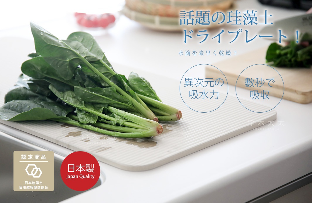 寬版米白色珪藻土置物墊，表面有排水溝槽，墊上有濕潤的綠葉蔬菜，背景為廚房水槽與木質砧板。