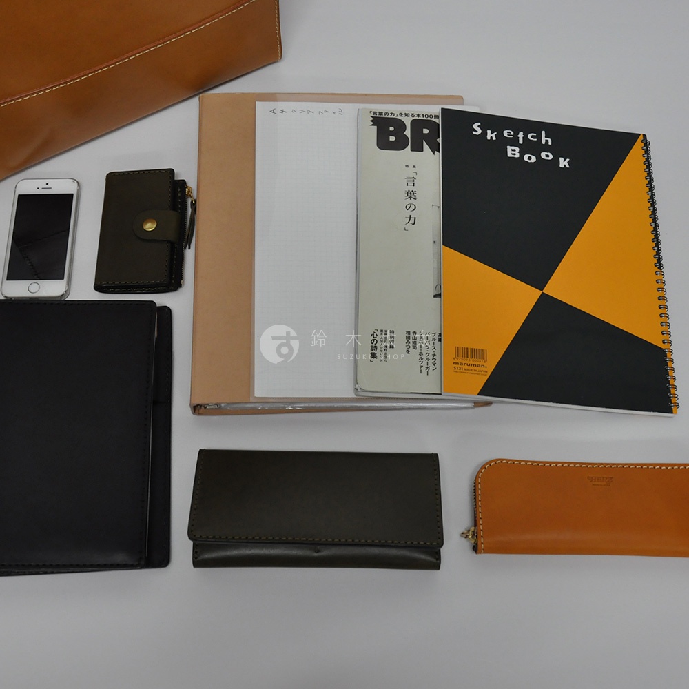 皮革直式托特包 T-44 L，搭配手機、卡夾、筆記本、筆記本和長夾，整體為棕色、黑色與墨綠色調。