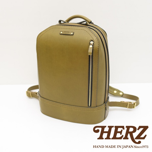 職人手作立體商務後背包，橄欖綠皮革材質，設有雙拉鍊主隔層及前方拉鍊袋，搭配金色拉鍊與扣環，展現簡約俐落的設計風格。