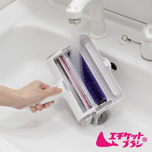 白色雙層除塵滾輪，內含粉色及紫色滾輪，置於白色水槽中，下方有水流通過，左手持握滾輪把手。