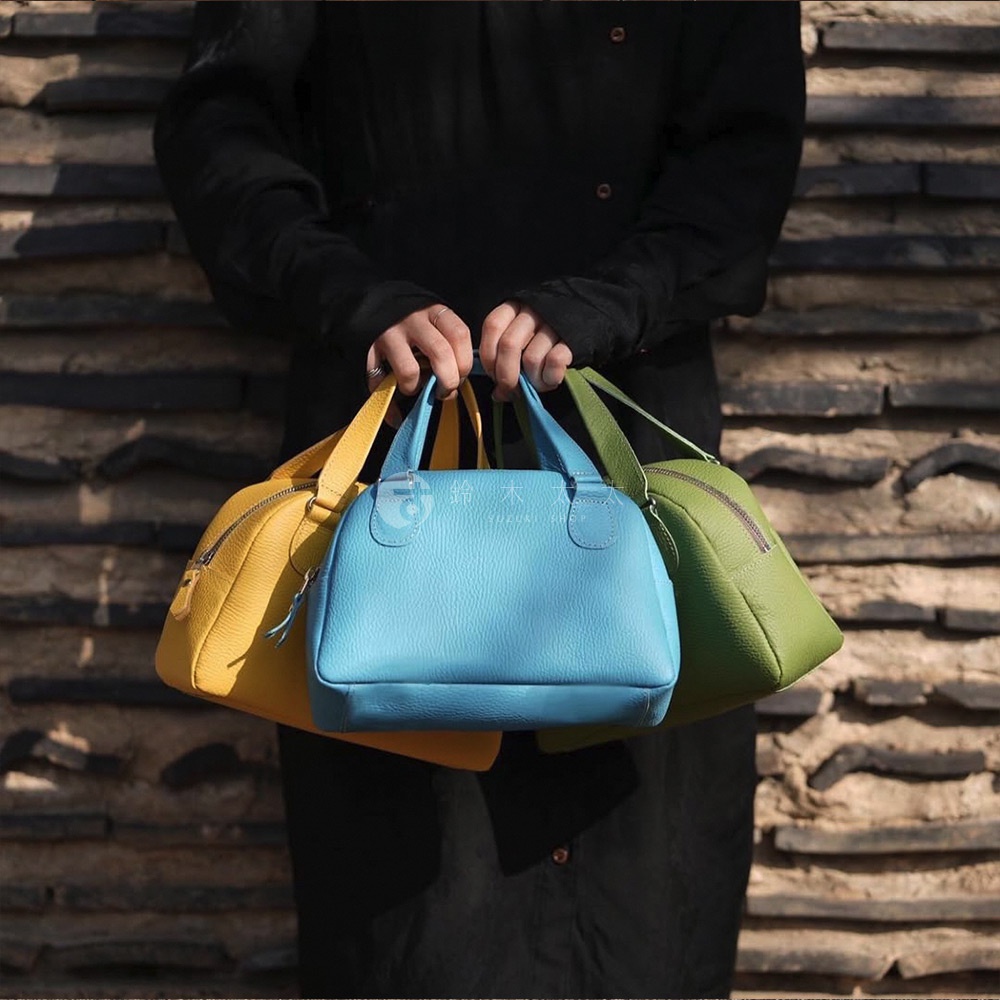 三款由皮革製成的迷你手提包，顏色分別為亮黃色、天藍色及草綠色，造型呈半月狀，皆配有雙提把。