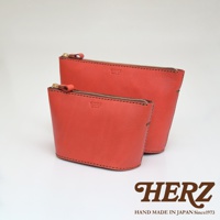 兩個橘紅色皮革製的職人手作三角收納包，一前一後擺放，材質呈現細緻皮革紋理，並配有金色拉鍊。