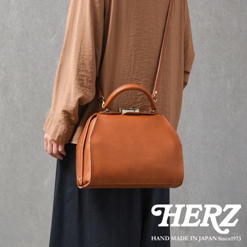 職人手作棕色皮革兩用口金手提包，簡約醫生包造型，配有頂部提把與可拆卸肩帶，金屬旋轉鎖扣，質感皮革紋理。