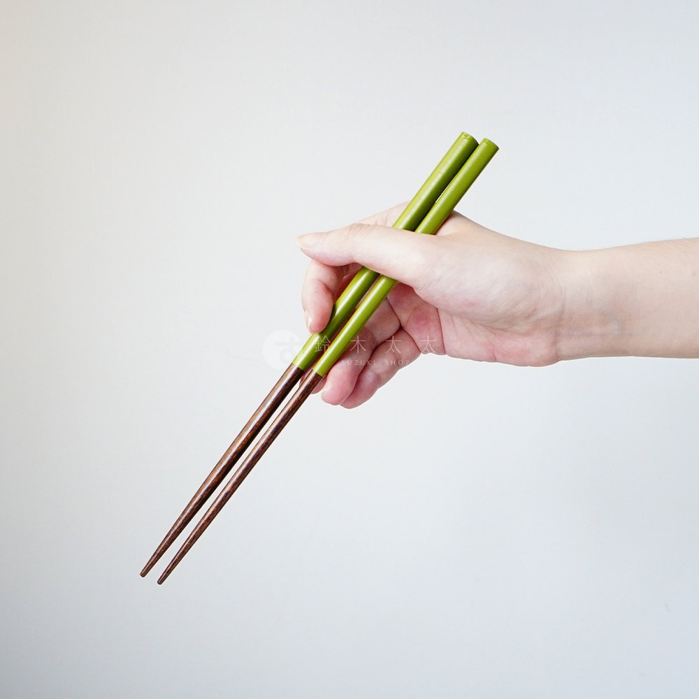 一雙現代原彩木筷，上端為鮮綠色，下端為木質原色，由一只手持握。