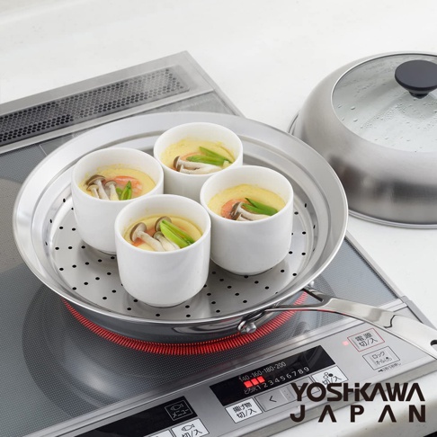不鏽鋼蒸鍋盤，盤中盛有四個裝有茶碗蒸的白色陶瓷杯，蒸鍋盤上有圓形透氣孔，盤旁放置一個透明玻璃蓋的銀色不鏽鋼鍋蓋，整體放在電磁爐上。