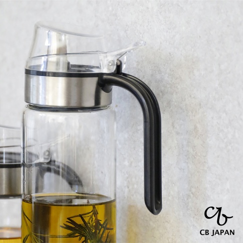 CB JAPAN atomico系列耐熱防回流玻璃油罐，罐內裝有金黃色食用油，並浸泡著幾枝迷迭香，搭配黑色手把。