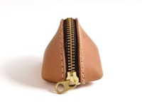 淺棕色皮革製成的貝殼造型零錢包，配有黃銅拉鍊，手工縫製，質感細緻。