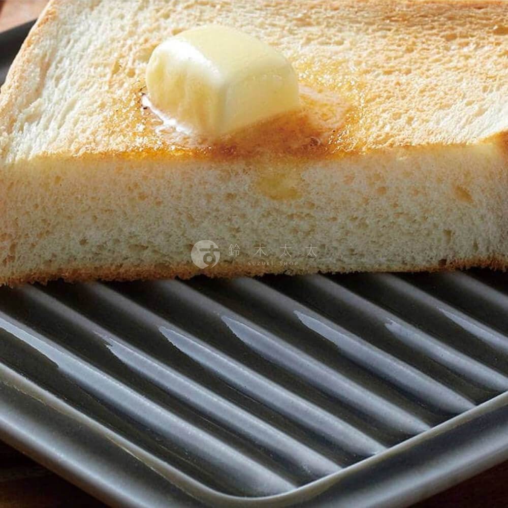 一片烤吐司上放著一塊融化的奶油，放在一個灰色素釉的美濃燒吐司酥脆專用盤上，盤子有著條紋設計。