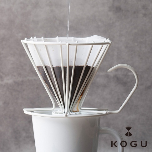 極簡白色鏤空線條日製18-8不鏽鋼咖啡濾杯，置於白色馬克杯上方，濾杯內有咖啡粉，上方正有水流下。