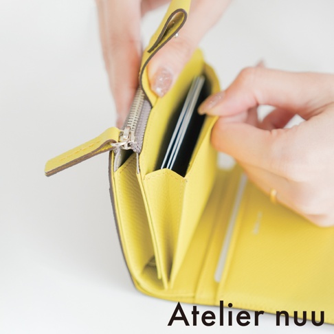雙手正打開一個亮黃色的 Atelier nuu 皮革 L 型拉鍊短夾，短夾內部隔層展示著存放的信用卡，展現其精緻的紋理與細節，畫面呈現溫潤的質感。