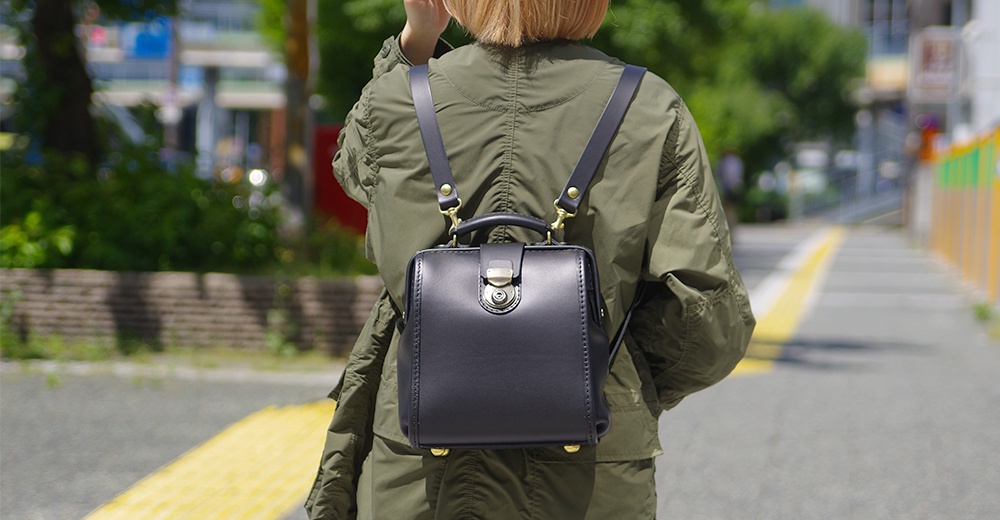 黑色皮革迷你後背醫生包，附有金色搭扣與提把，兩條皮革肩帶。