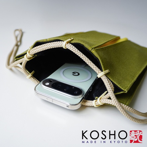 橄欖綠色帆布材質的京都KOSHO ougi信玄袋，袋口以米色編織繩與繩扣開合，內部放入一支裝有磁吸充電環的手機，整體呈現簡約質感與日式工藝風格。
