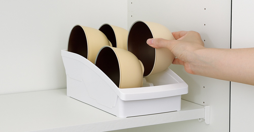 手正將一個淺米色碗放入白色櫥櫃式餐碗收納架中，收納架內已擺放有三個相同的碗。