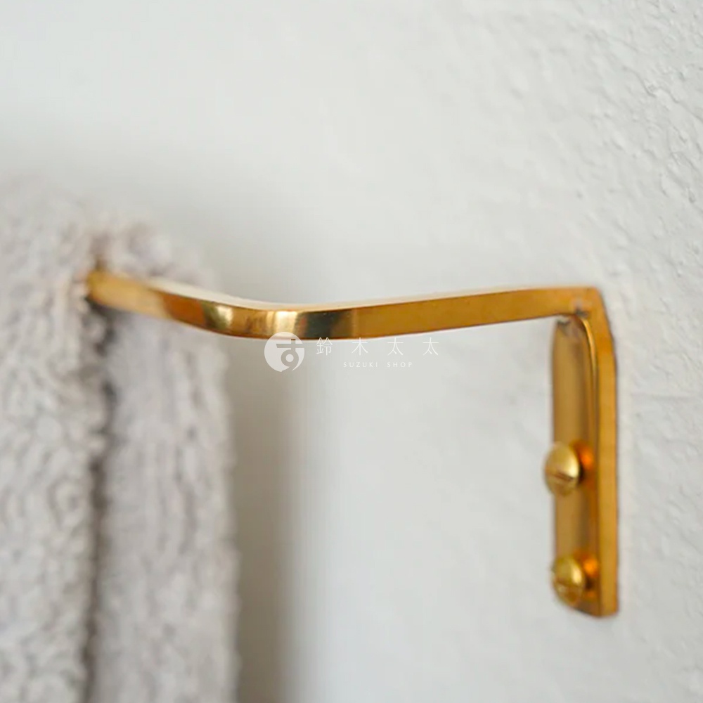 黃銅單桿毛巾架，金屬材質，表面光滑，呈金色，一端固定於牆面，另一端懸掛著一條淺灰色毛巾。