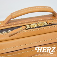 職人手作皮革兩用多功能收納單肩包，展示皮革提把、金色拉鍊與縫線細節，材質為天然皮革，顏色為棕褐色。