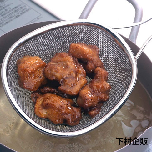 一個橢圓形的不鏽鋼料理小濾網，網面細密，網邊和手柄為銀色不鏽鋼材質，濾網內盛有數塊金黃色的炸物，淋有深棕色醬汁。