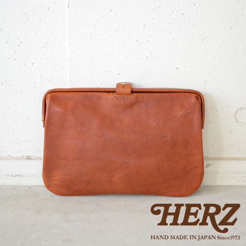 棕色皮革製成的職人手作Organ手拿包，採用簡約的設計，頂部有皮革搭扣和縫線細節，質感溫潤。