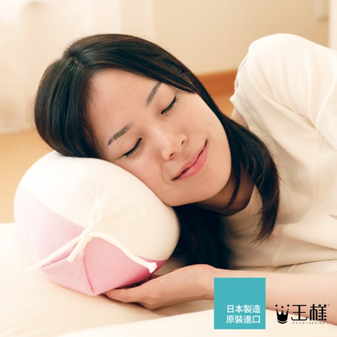 一名女子側臥，臉頰輕靠在一個圓形糖果造型的枕頭上。枕頭為粉紅色與白色拼接設計，表面柔軟，並有白色細繩繫成蝴蝶結。