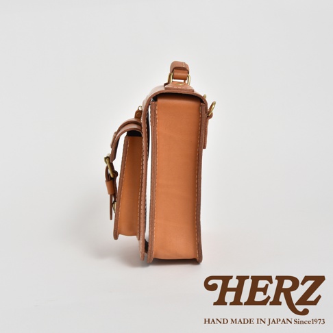 淺棕色職人手作皮革立體口袋兩用單肩包，側邊視角，包身結構清晰，帶有金屬扣環和皮革揹帶。