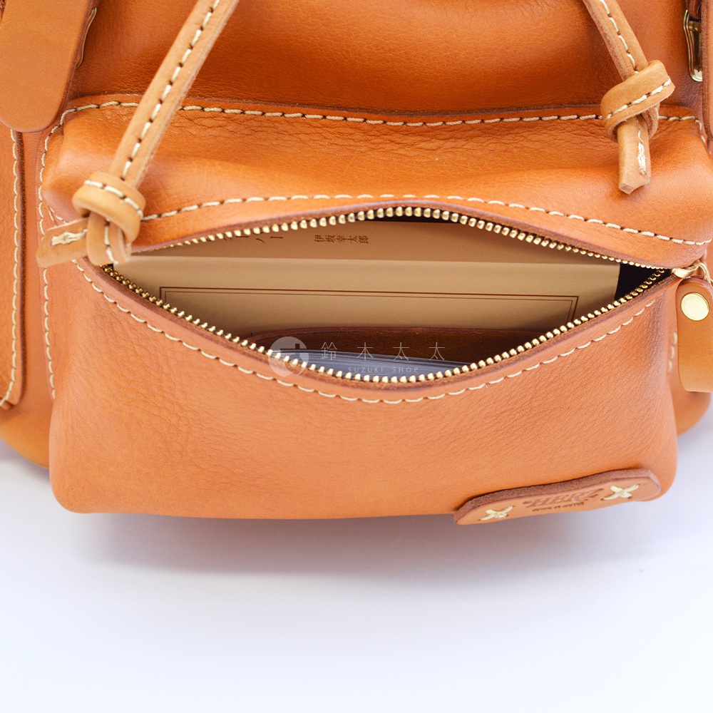 棕色皮革復古風旅行後背包，拉鍊打開，露出內部有書本和卡片夾，包包外部有白色縫線裝飾。