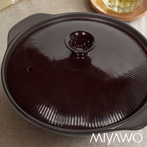 深棕色陶土湯鍋，鍋蓋帶有放射狀紋路及圓形把手，鍋緣有兩個提把，鍋蓋上有一小孔。