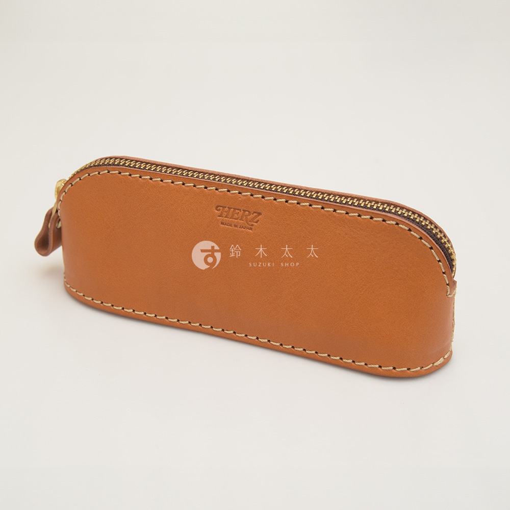 職人手作皮革三角弧形收納筆袋，淺棕色皮革，金色拉鍊，縫線清晰，側面印有品牌Logo和日文店名。