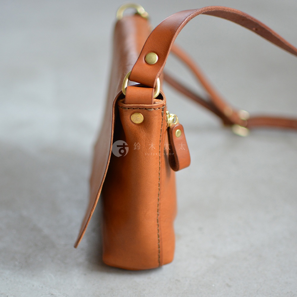 一個棕色皮革製成的斜背包，有著金色的拉鍊和縫線細節，從側面拍攝。