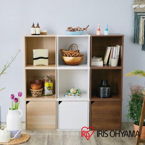 展示一個由九個立方體組成的收納櫃，其中三個立方體下方帶有門。收納櫃的顏色有原木色、白色和深棕色。櫃內擺放著書籍、籃子、裝飾品和植物。