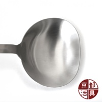 不鏽鋼萬用料理大勺，勺頭為圓弧形，表面呈現金屬光澤，手柄為長條狀，材質為不鏽鋼。右下角有紅色圓形標誌，內有四個中文字。