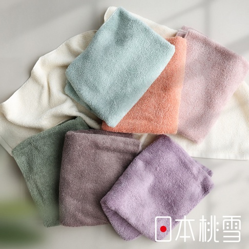 一張俯視角度拍攝的照片，展示了多條色彩柔和、質感蓬鬆柔軟的日本桃雪精梳棉飯店浴巾，浴巾以堆疊的方式交錯放置，包含白色、淡綠色、橘粉色、粉紫色、深綠色、深灰紫色與亮紫色，右下角印有日本桃雪的品牌標誌。