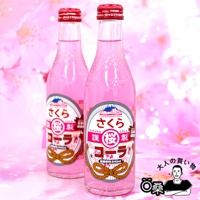 兩瓶粉紅色玻璃瓶裝的期間限定汽水，瓶身印有日文「さくらコーラ」和富士山圖案，搭配紅色瓶蓋。