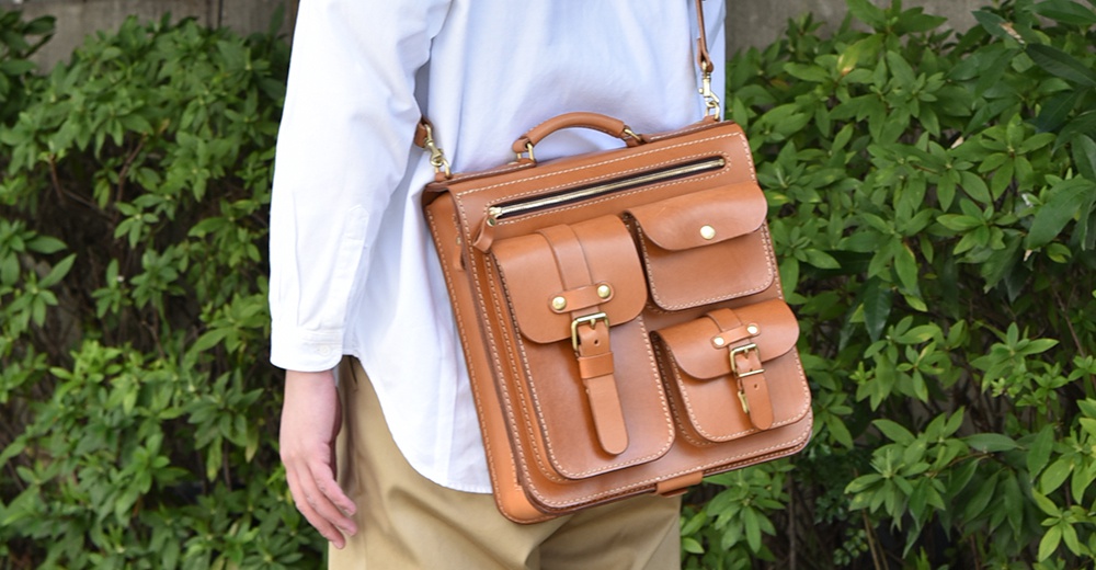 職人手作皮革三口袋三用後背包，以棕褐色皮革製成，設有拉鍊主袋、兩個磁釦翻蓋前袋及一個帶有皮帶釦的翻蓋前袋。