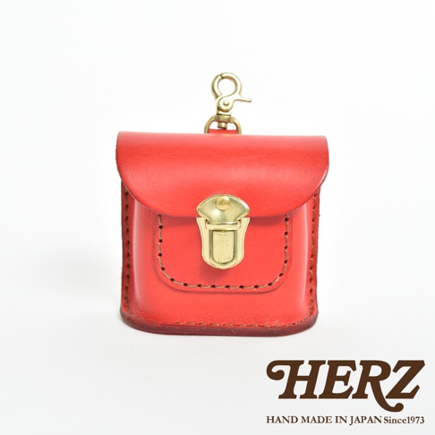 紅色職人手作皮革耳機收納包，帶有黃銅色金屬釦和掛環，皮革表面有縫線裝飾。