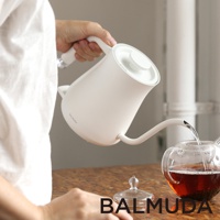 手持白色簡約手沖壺，壺嘴細長，正在往透明玻璃茶壺中注入熱水。