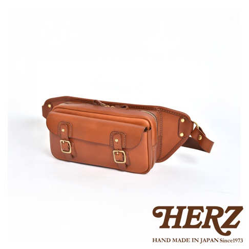 職人手作皮革騎士隨身斜背包，採用棕色光滑皮革製成，設有兩個帶有金屬釦的翻蓋口袋，以及一個拉鍊主隔層。