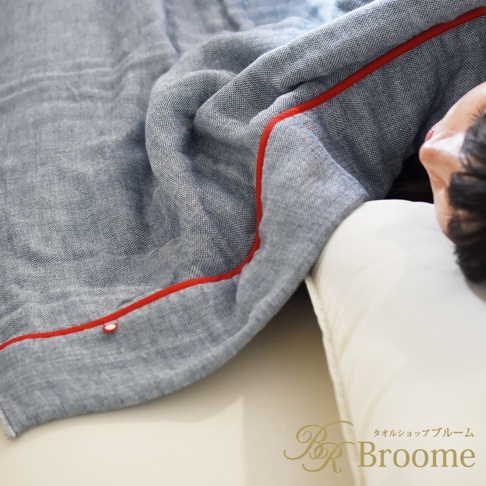 一條藍灰色五層紗材質的四季被，邊緣滾有紅色滾邊。