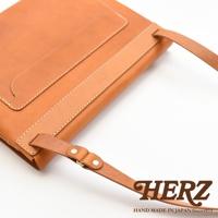 職人手作皮革經典郵差包，採用棕褐色皮革，搭配同色系皮革飾條與縫線，設計簡潔，肩帶以黃銅釦件固定。