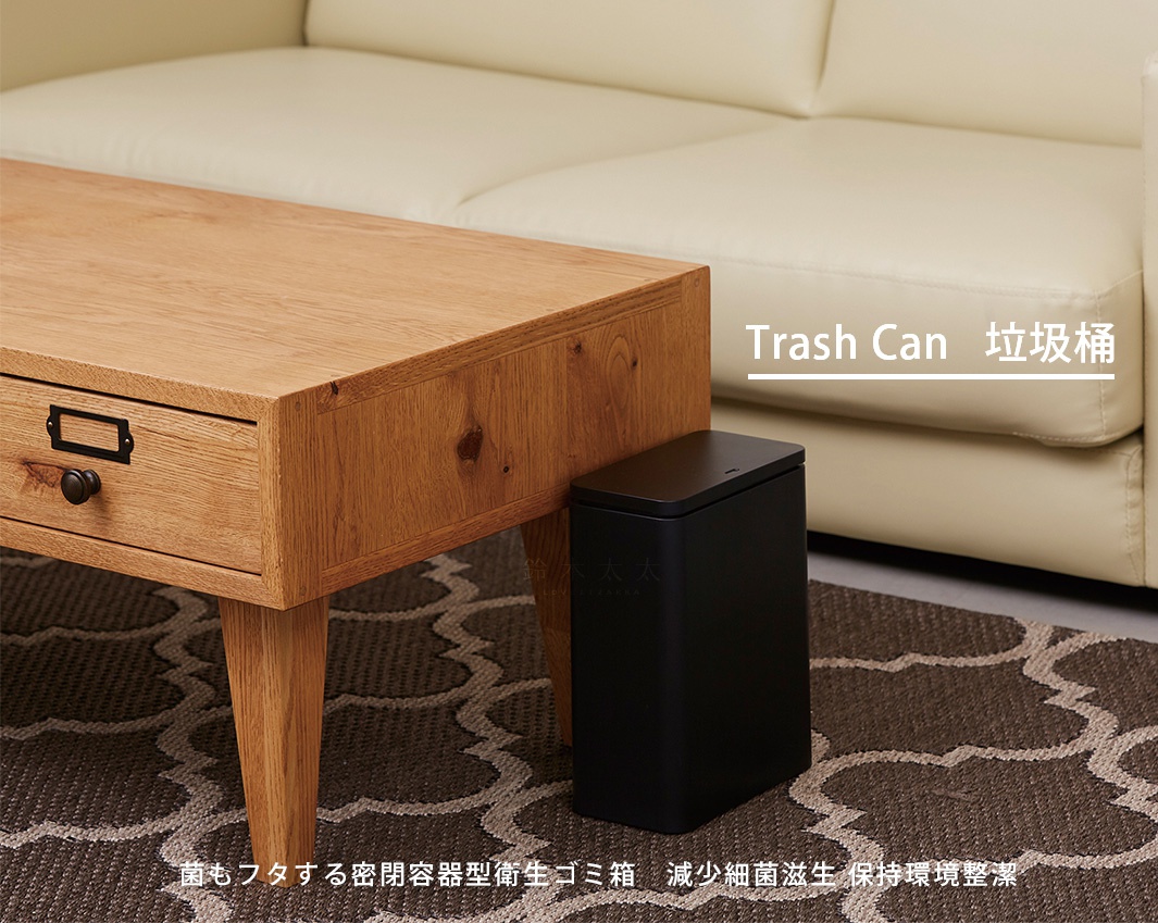 黑色方形按壓式垃圾桶，置於木製桌邊，搭配米白色沙發和地毯，簡約實用。