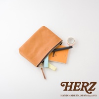 職人手作皮革長方形拉鍊收納包，材質為皮革，顏色為自然棕色，拉鍊為深色，包內裝有筆、筆記本和便利貼，旁邊有一個小卷筒膠帶。