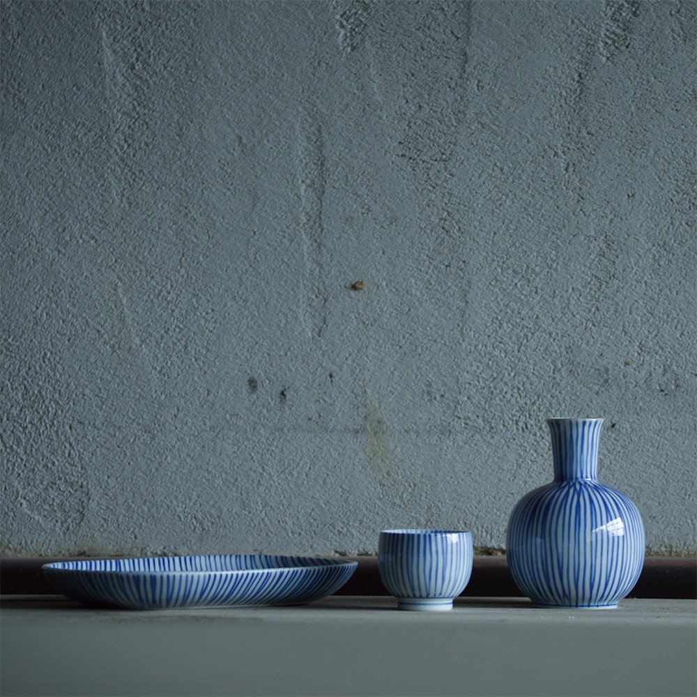 波佐見燒十草紋小豆皿，藍白條紋陶瓷，包含一個扁平的盤子、一個杯子和一個瓶子，擺放在灰色背景上。