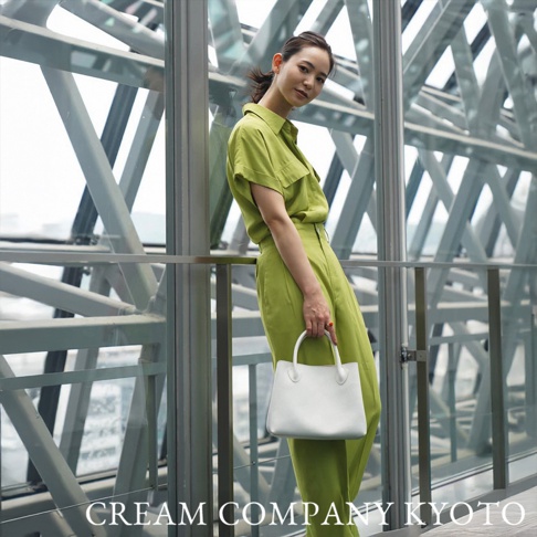 一位女性手持白色皮革兩用手提托特包，包身簡潔，有短提把和可拆卸長背帶，搭配綠色套裝。