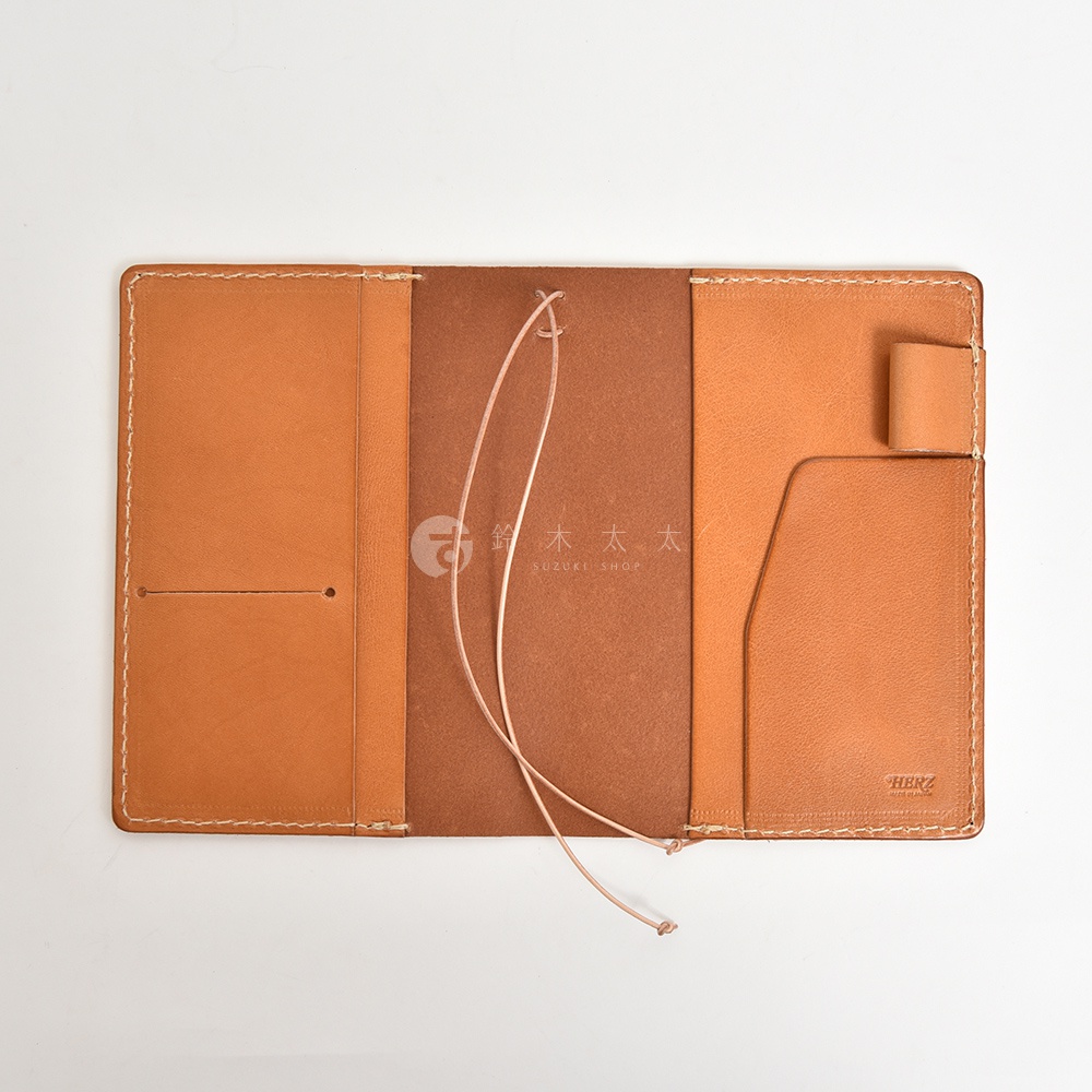 這是一本打開的皮革手帳書套，內側為淺棕色皮革，有卡片夾層和筆套，中間為深棕色內襯，並附有彈性綁繩。
