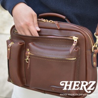 職人手作皮革兩用多功能收納單肩包，採用咖啡色皮革，設有頂部提把、多個拉鍊隔層和前置口袋，搭配金色拉鍊和五金配件，展現精緻工藝。