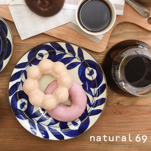 藍白花紋圓盤上擺放著兩個日式甜甜圈，一個為淺粉色，另一個為米白色，盤子邊緣有金色滾邊，盤子旁還有咖啡和咖啡壺。