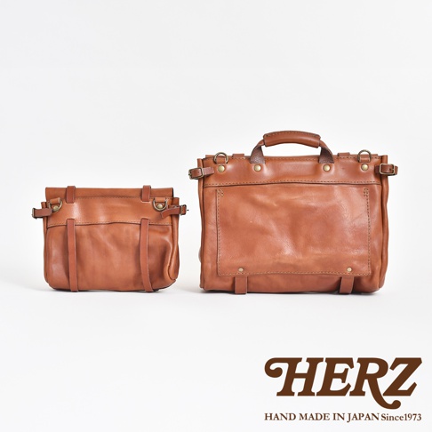 兩款復古棕色鞣革郵差包，一較小，一較大，皆採用水洗加工處理，展現皮革自然紋理與質感，並配有金屬扣環與皮帶裝飾。